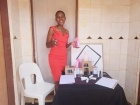 Young woman wearing a red dress standing next to a little both presenting her perfume business
