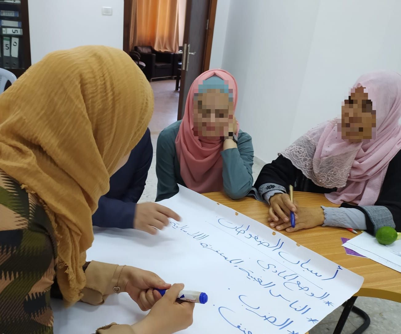 women with faces blurred working together around a table, writing on a big piece of paper