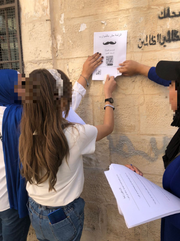 Young women with faces blurred putting a flyer up on a wall outside