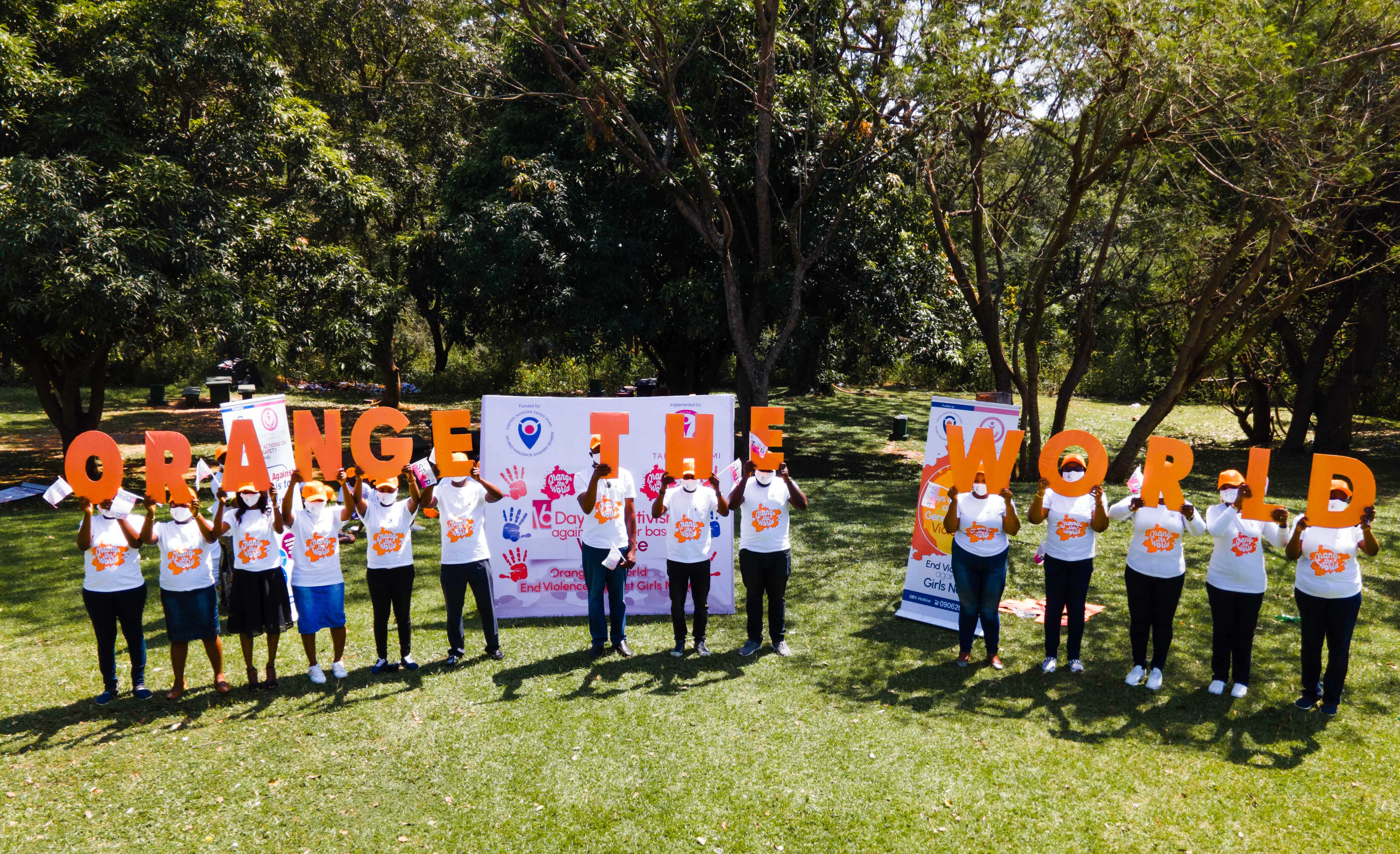 Group of people standing in a yard holding up big orange letters that read Orange the World