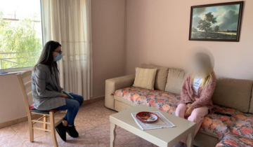 Two women seen discussing in a room while seated in a chair and a couch