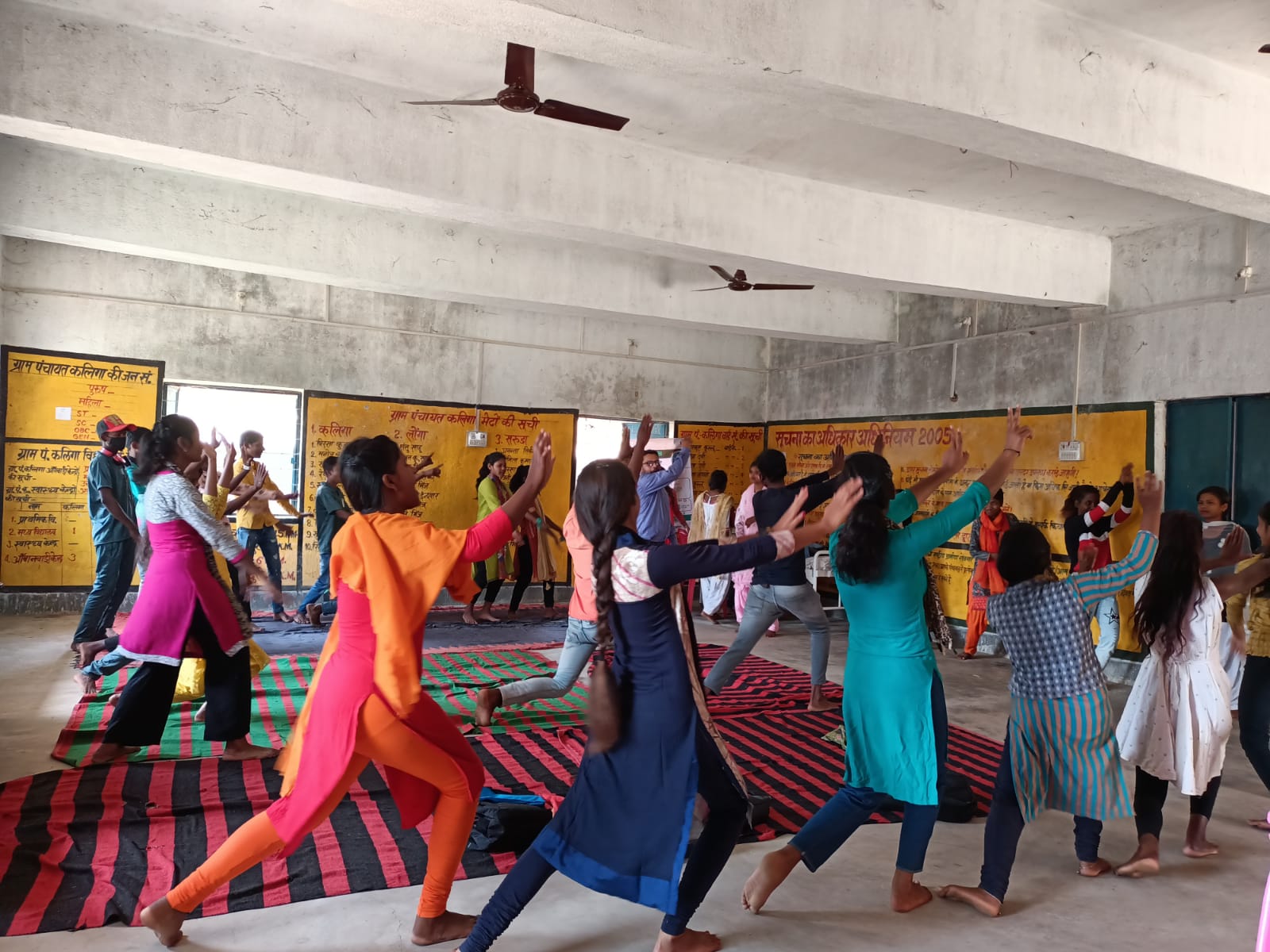 Group of women seen dancing with their hands up in a room. They are wearing colourful garments.