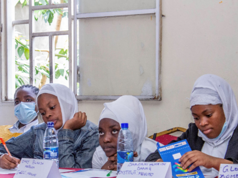 Young black schoolgirls wearing white veil on their head are sitting at their desk in a classroom.