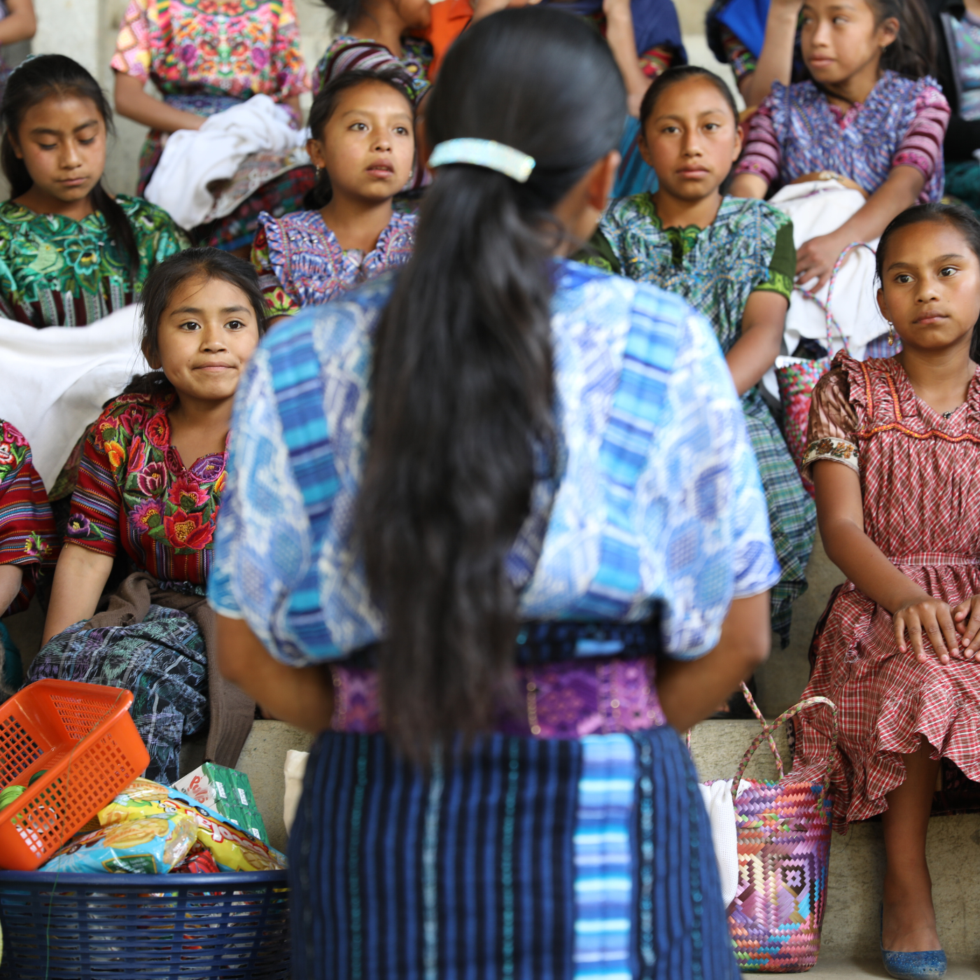 Guatemalan woman seen from the back standing in front of a large group of young women