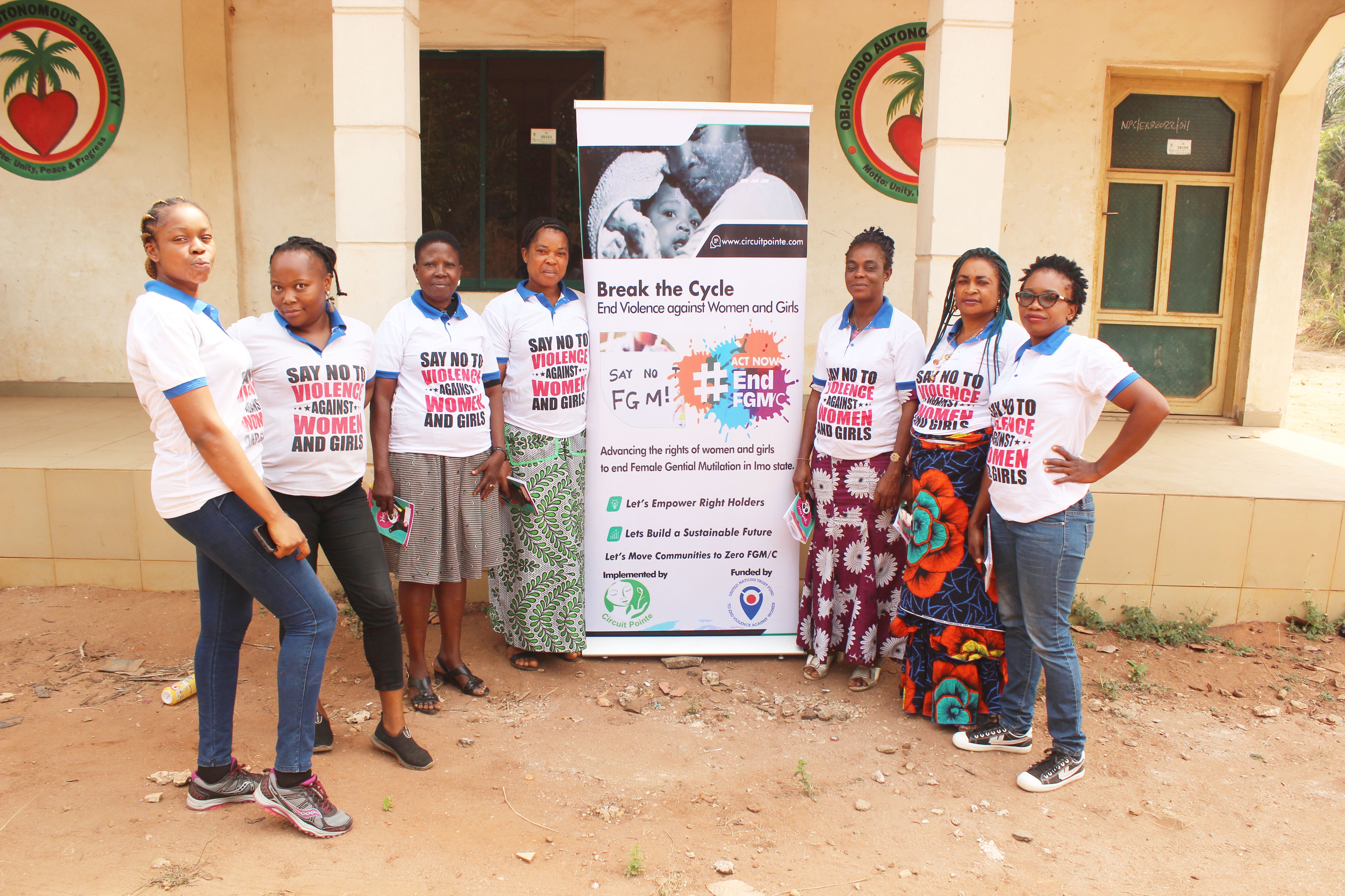 Group of seven black women standing outside a building, gathered around a banner that reads "Break the cycle: end violence against women"