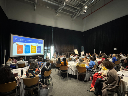 Group of participants in a room watching a presentation on a big screen and listening to speakers