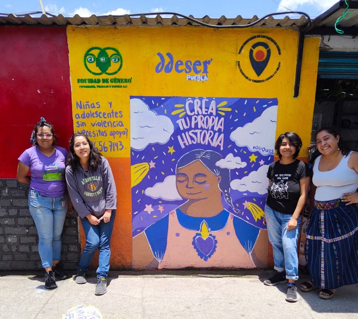 Group of 4 women, 2 by 2, posing for a photo in front of a colourful mural depicting women's rights