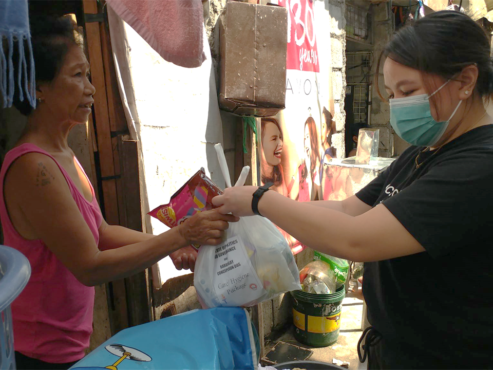 Photo shows two women, one from IPG gives emergency relief kit to another woman in the community affected by COVID-19