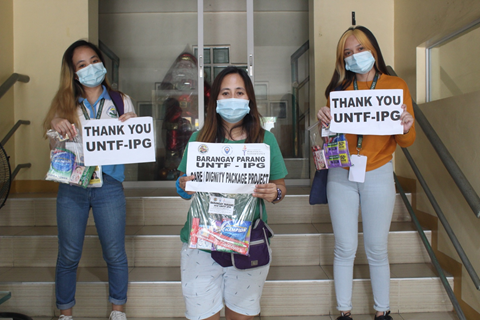 Women and girls who are receiving help from IPG are photographed with relief kits from the organization during COVID-19. The photo consists of 3 women holding a kit and a sign that reads "Thank you UNTF-IPG"