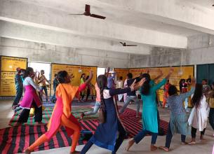 Group of women seen dancing with their hands up in a room. They are wearing colourful garments.