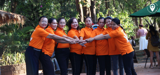 Group of women wearing orange t-shirts outside all joining hands in the middle